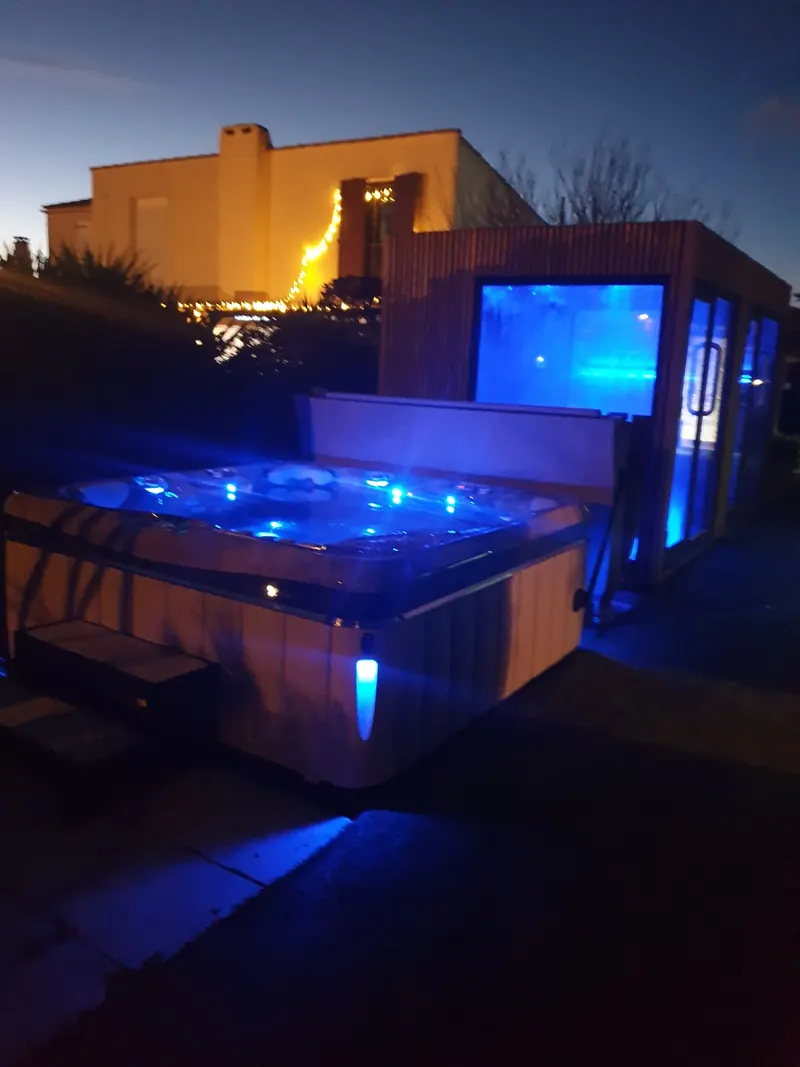 Spa de nuit sous éclairage LED bleu, avec la maison illuminée