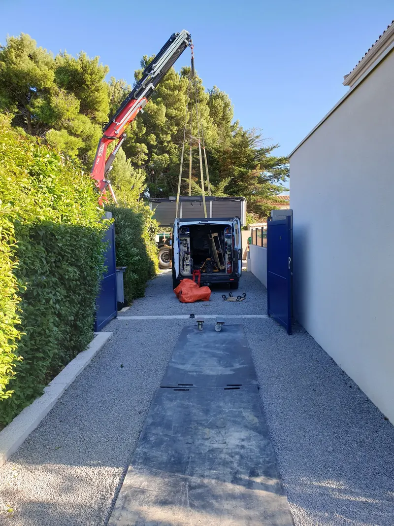 Spa gris suspendu à une grue au-dessus d'une camionnette, dans l'allée gravillonnée d'une maison à Mèze