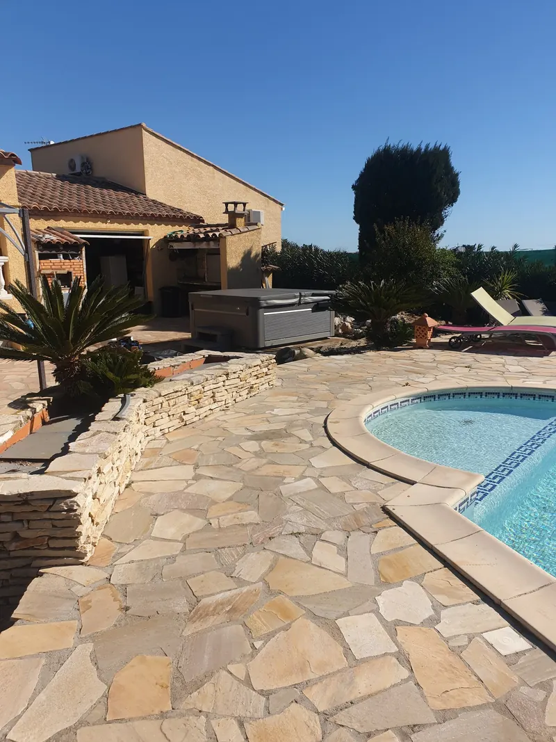 Spa gris sous sa couverture, près de la maison, au-delà d'une terrasse en pierres et d'une piscine à Mèze