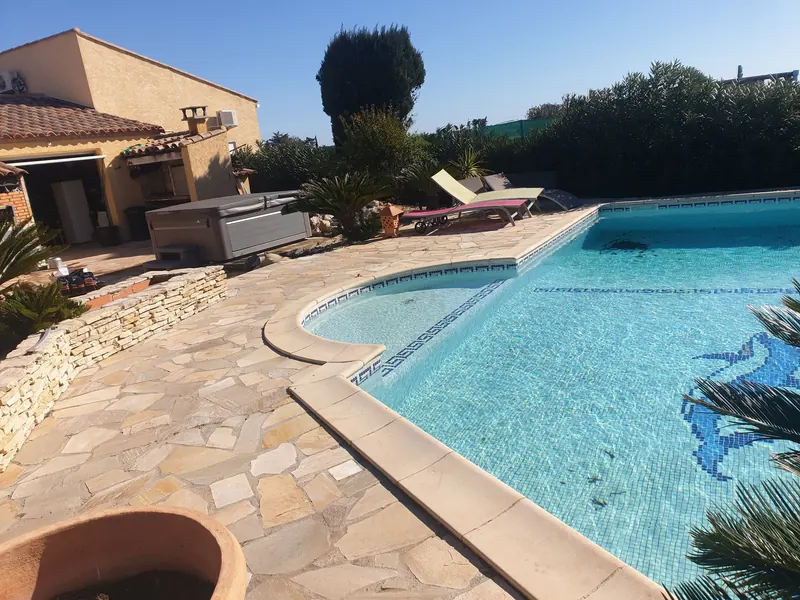 Terrasse en pierres et piscine, avec le spa gris installé contre la maison à Mèze