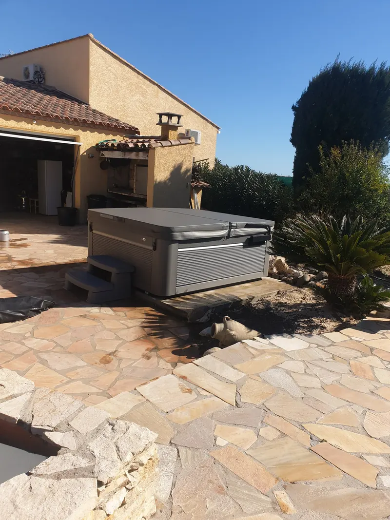 Spa gris avec marchepied, posé sur une dalle en bord de terrasse à côté d'un massif de cycas, à Mèze