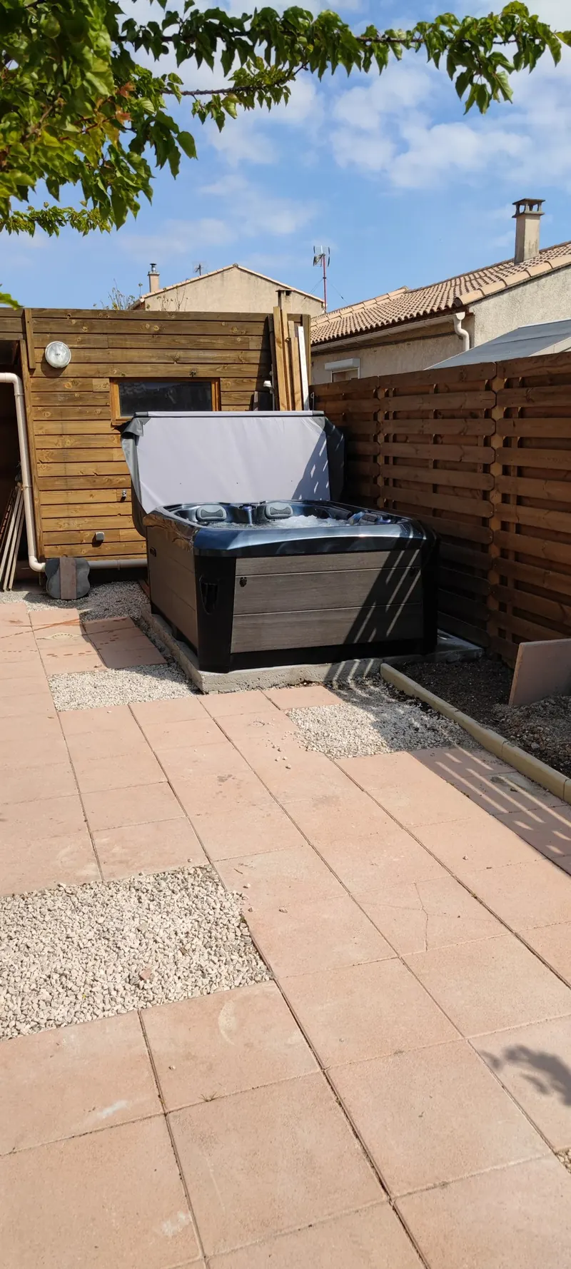 Spa fermé dans un patio clos, clôture en bois, bâtiment aux tuiles visible
