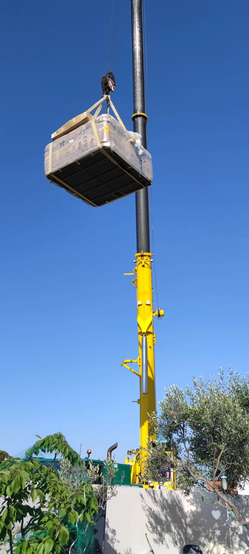 Spa blanc suspendu à la grue au-dessus du sol, végétation alentour