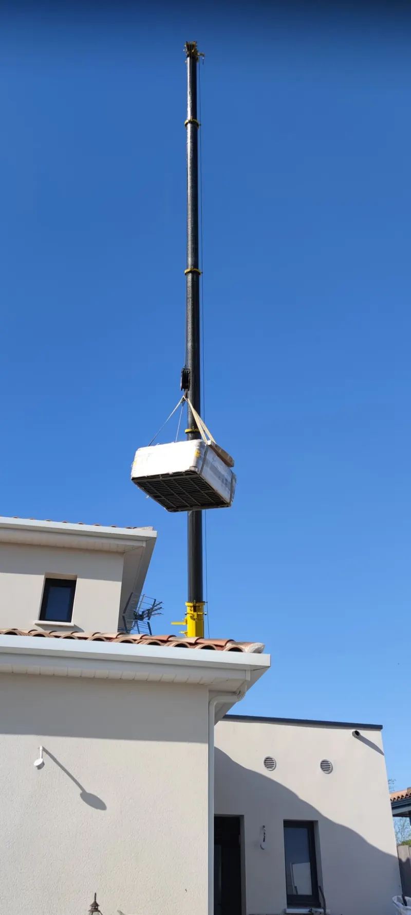 Spa blanc suspendu à la grue au-dessus d'une maison blanche, levage en cours