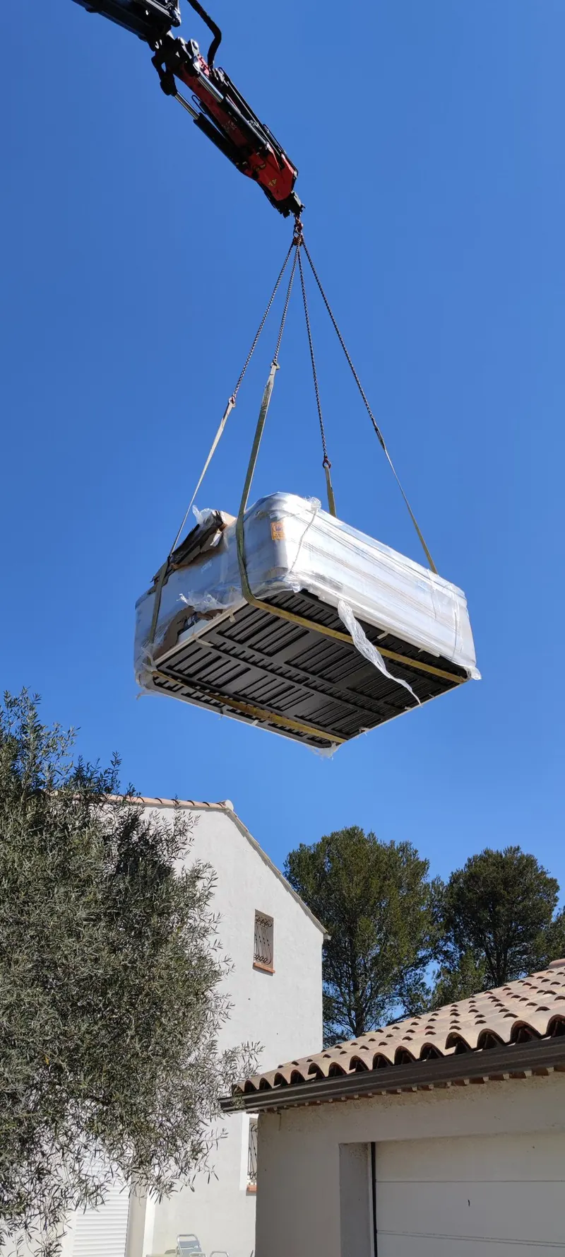 Vue aérienne du levage : spa suspendu, grue rouge en haut, cour en dessous