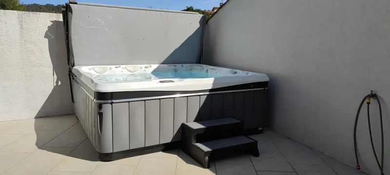 Spa gris et blanc en place en extérieur, dalle de béton, marches d'accès noires