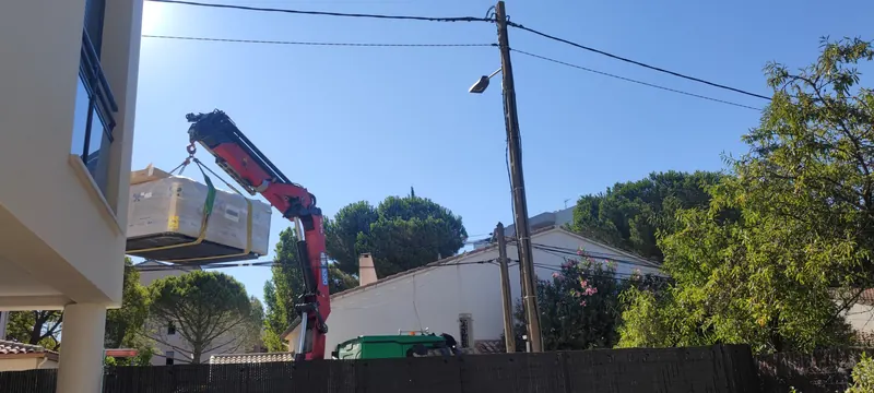Spa blanc soulevé par la grue rouge, jardin en dessous