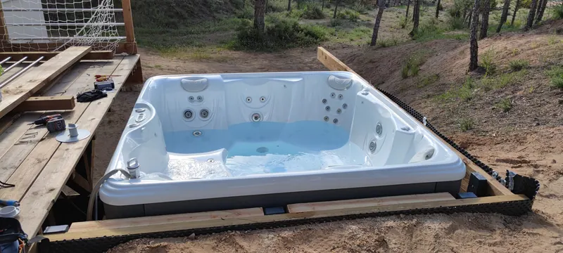 Spa à coque blanche encastré dans un cadre en bois, terrasse en chantier à gauche