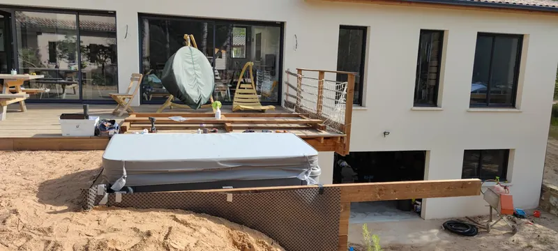 Spa sous son couvercle gris dans son cadre en bois, devant la façade d'une maison