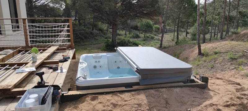 Spa à coque blanche, couvercle à demi relevé, pins et terrain sableux autour