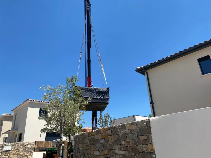 Spa suspendu à la grue au-dessus du patio, murs de pierre au premier plan