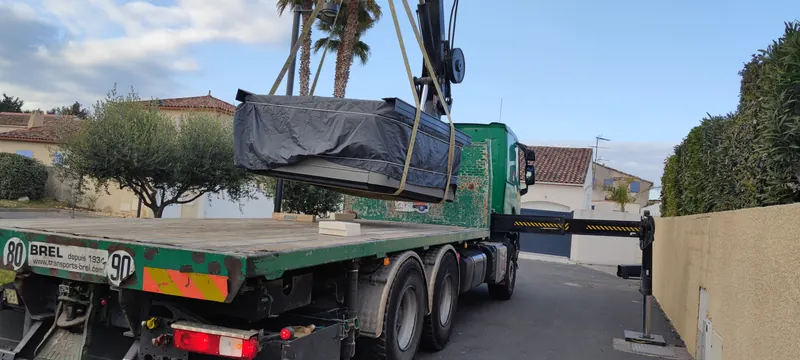 Spa soulevé hors du plateau du camion par les sangles de la grue