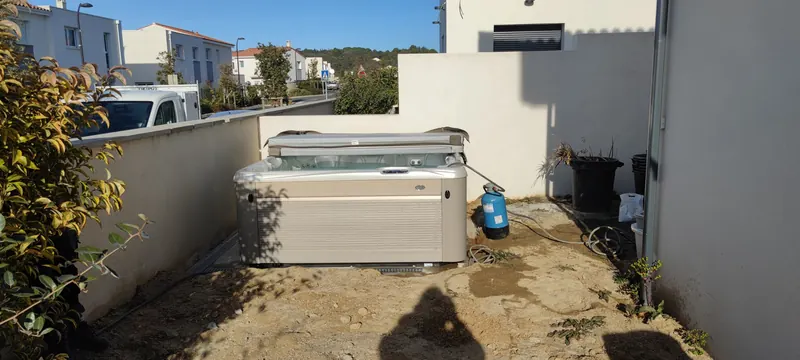 Spa couvercle relevé dans un passage étroit entre deux murs, cylindre bleu relié par un tuyau