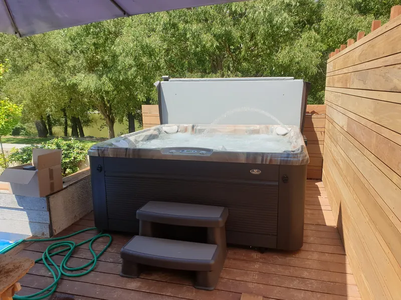 Spa en eau sur une terrasse en bois, contre un brise-vue, devant des arbres à Saint-Bauzille-de-Putois