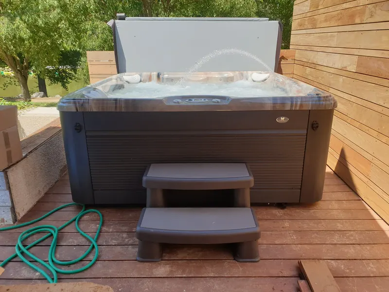 Spa vu de face, couvercle relevé et marchepied devant, sur une terrasse en bois à Saint-Bauzille-de-Putois