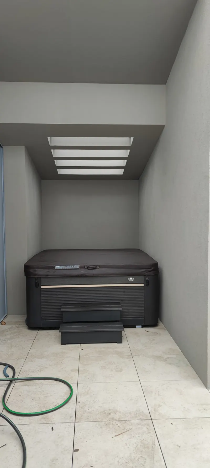 Spa noir dans un petit abri couvert, avec escalier d'accès et dalle béton
