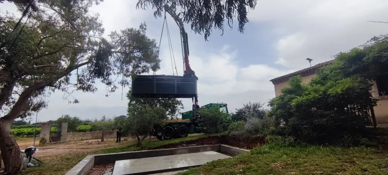 Gros plan du spa noir posé sur sa fondation en béton, grue encore attachée