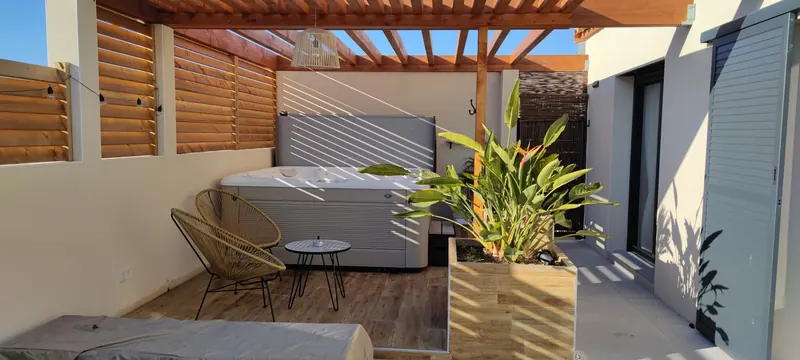 Spa sous la pergola en bois, deux fauteuils en rotin et grande plante au premier plan