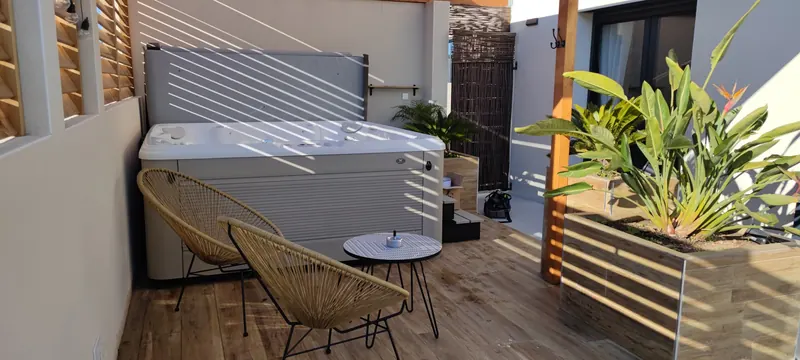 Spa couvercle relevé contre le mur, fauteuils en rotin et table ronde devant