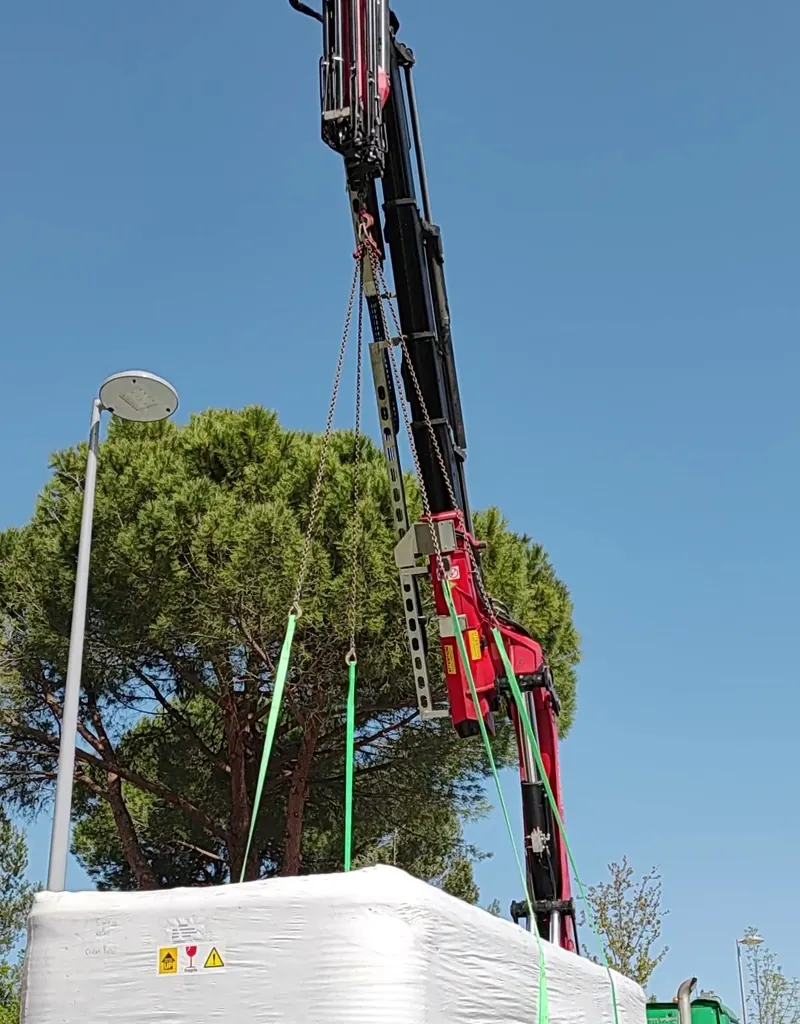 Spa emballé de blanc soulevé par la grue du camion, pins au fond