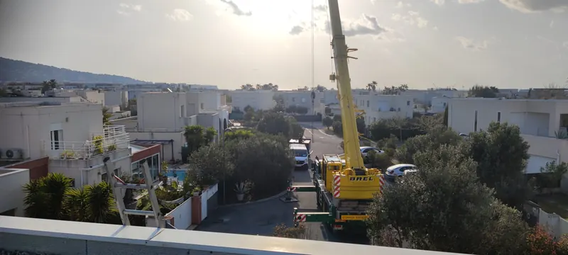 Grue jaune soulevant le spa, vue aérienne sur les maisons blanches