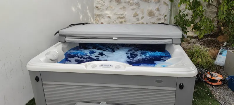 Spa blanc et gris installé dans un jardin, avec un mur de pierre et du lierre