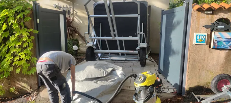 Spa debout sur un chariot de manutention, portail ouvert, personne penchée sur un coussin gris