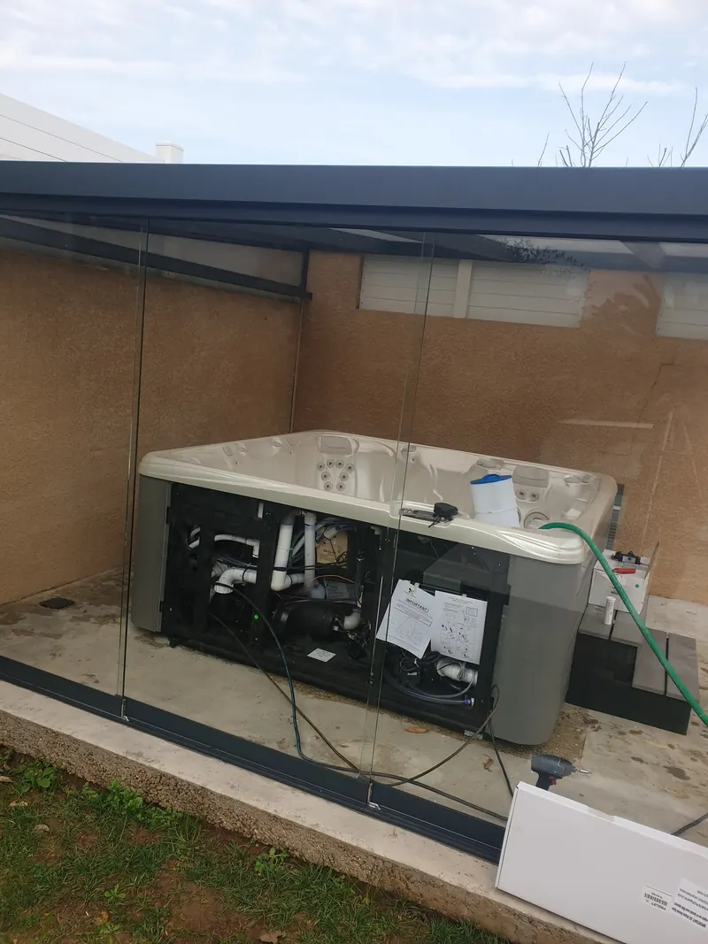 Pompes et tuyauterie du spa à nu, tuyau d'arrosage dans la cuve, sous la pergola vitrée